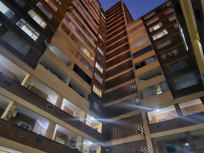 Low-angle view of a multi-story apartment building facade featuring brickwork, balconies, and decorative breeze block architectural elements at dusk.