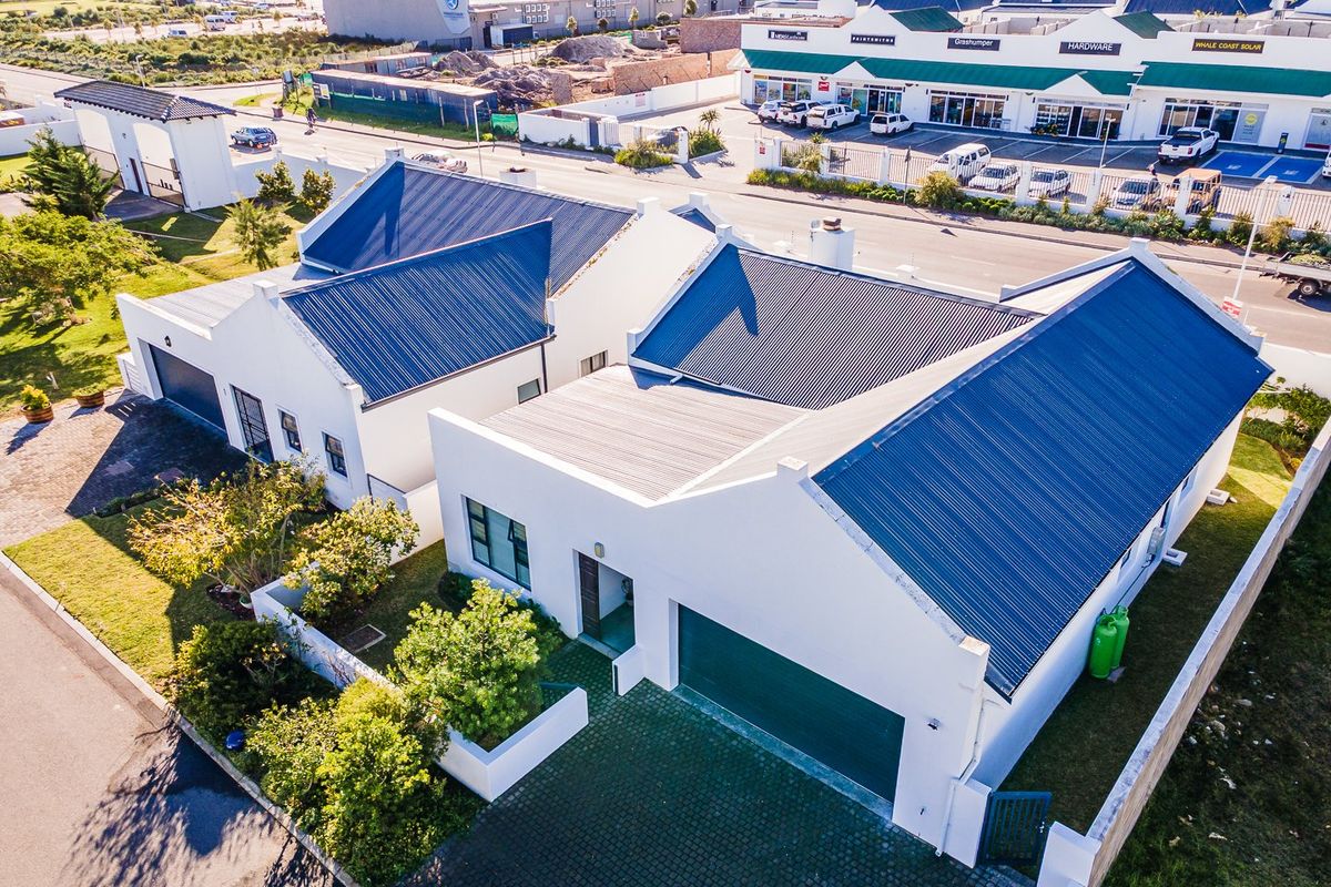 Aerial view of a modern residential property featuring a dark metal roof, double garage, and paved driveway within a secure estate setting.