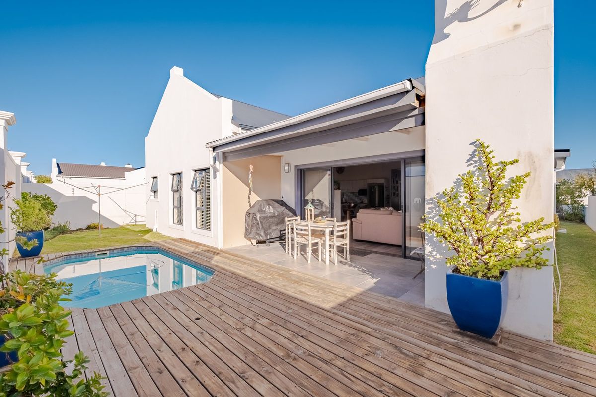 Rear exterior view featuring a swimming pool, timber decking, and a covered patio area with direct access to the home through sliding glass doors.