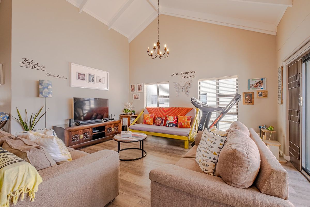 Spacious living room featuring a high vaulted ceiling with exposed rafters, a classic chandelier, and sliding glass doors leading to the exterior.