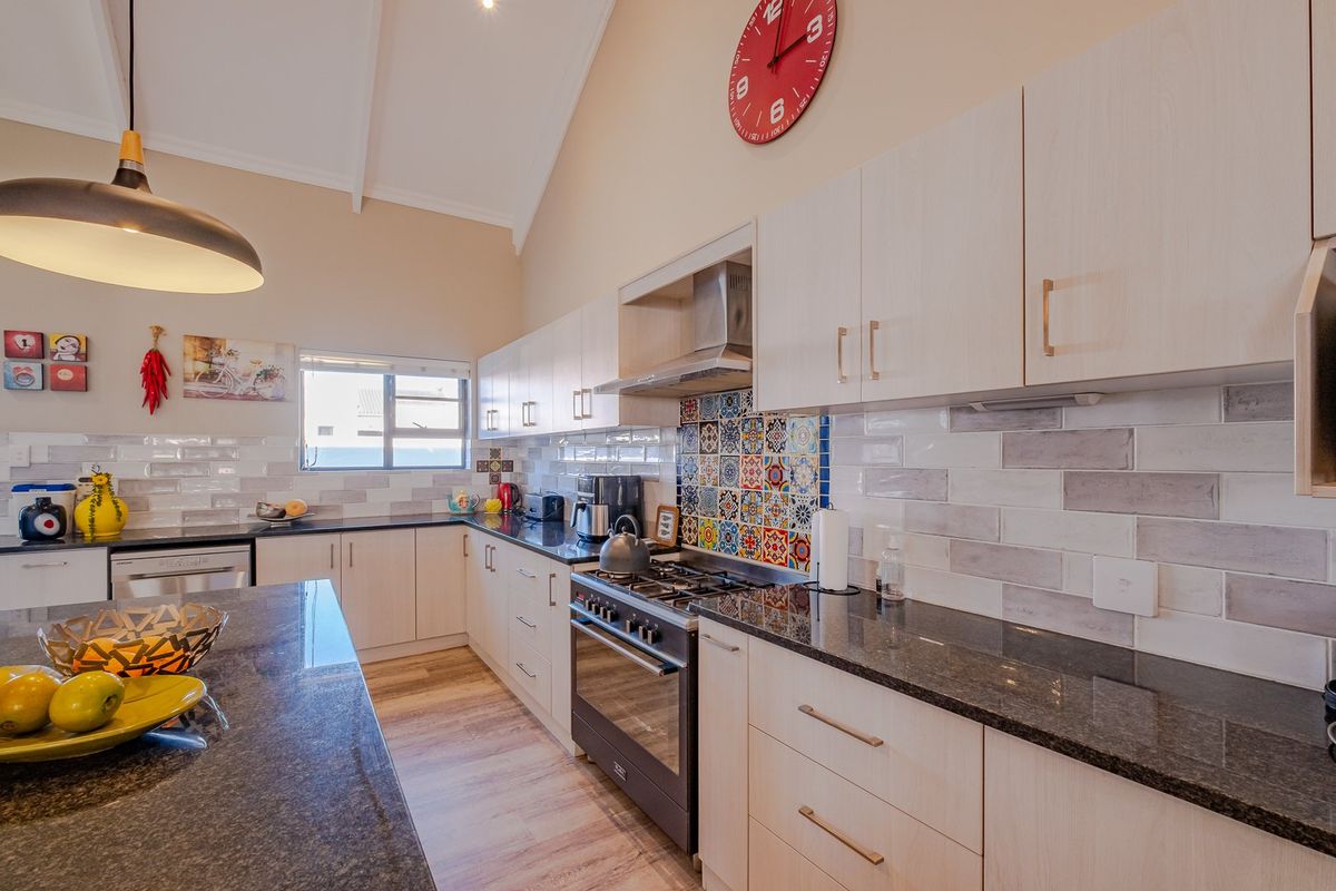 Modern kitchen featuring light wood cabinetry, granite countertops, gas stove with extractor, and a striking decorative tile backsplash under a high vaulted ceiling.