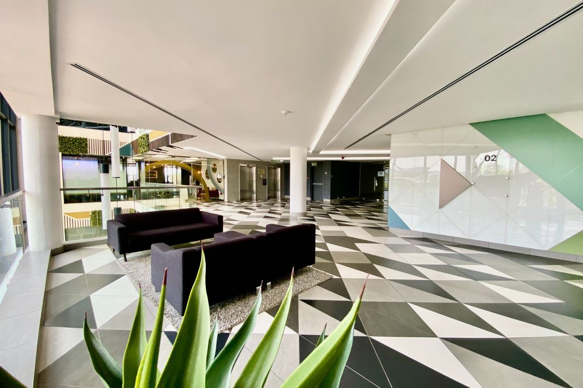 Modern commercial building lobby featuring high ceilings, geometric tiled flooring, and elevator access in a well-maintained, professional environment.