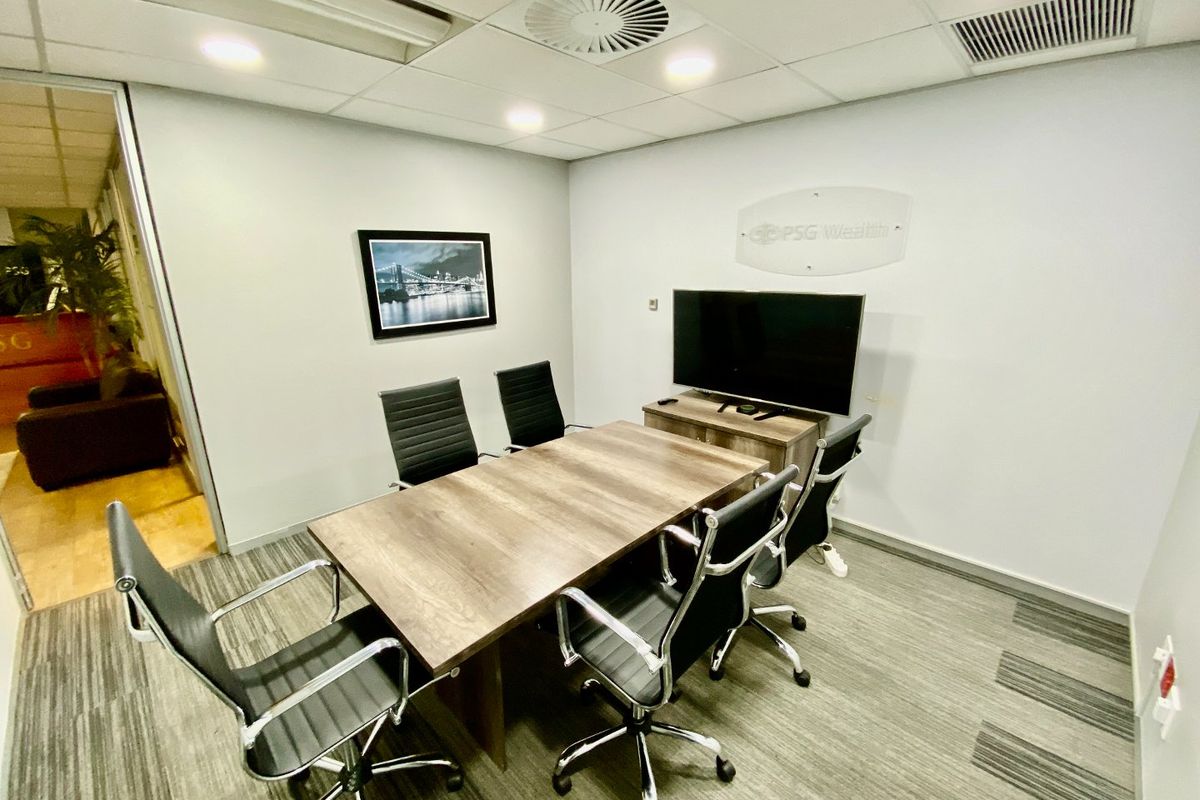 A professional commercial meeting room featuring a suspended ceiling, recessed lighting, air conditioning, and carpeted flooring, enclosed by a glass partition.