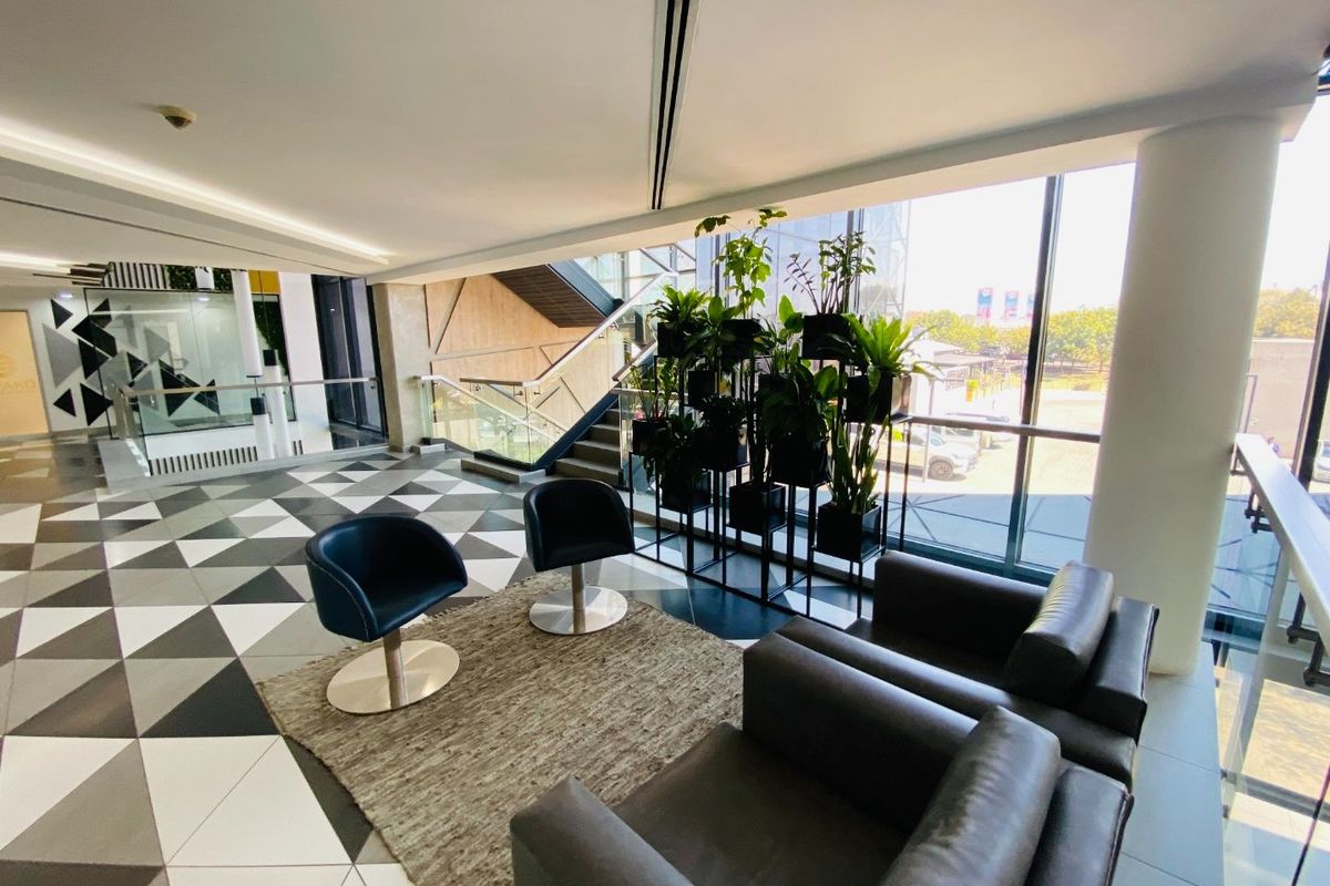 Modern commercial lobby or lounge area featuring floor-to-ceiling windows, geometric tiled flooring, and a glass-railed staircase.