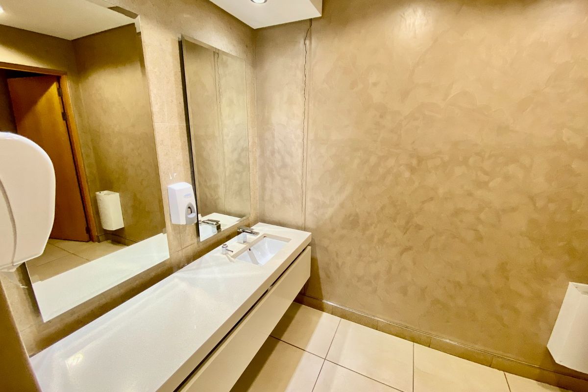 A commercial bathroom featuring a wall-mounted vanity with an integrated basin, large mirror, and tiled flooring, showing a visible vertical wall crack.