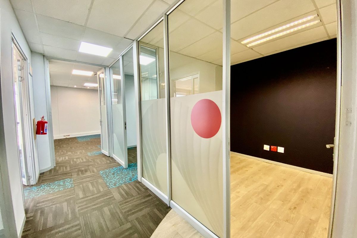 Modern commercial office space featuring glass partitioning, suspended ceilings, and a mix of carpet and laminate flooring in a clean, vacant layout.