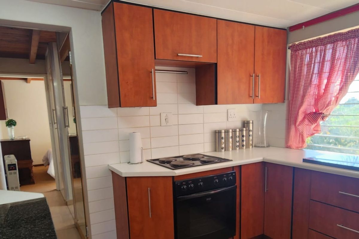 A functional kitchen featuring wood-finish cabinetry, a built-in oven and hob, tiled backsplash, and a window with security bars overlooking the exterior.