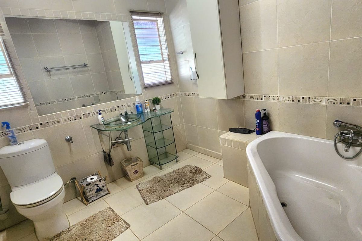 A functional bathroom featuring a built-in bathtub, toilet, wall-mounted vanity cabinet, and neutral tiled finishes throughout.