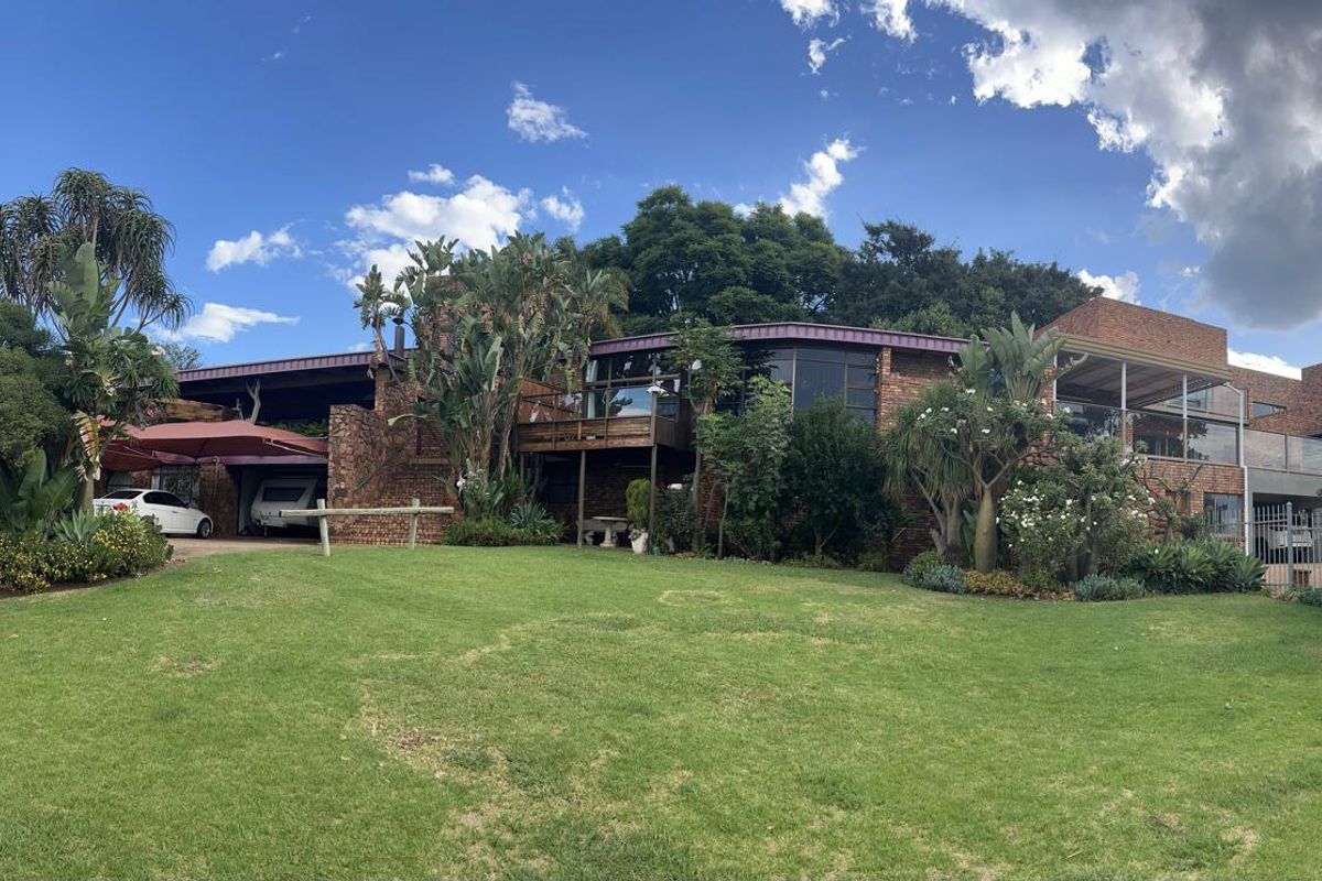 A spacious rear exterior view of a face-brick farm property featuring a raised wooden deck, large windows, and an expansive landscaped garden.