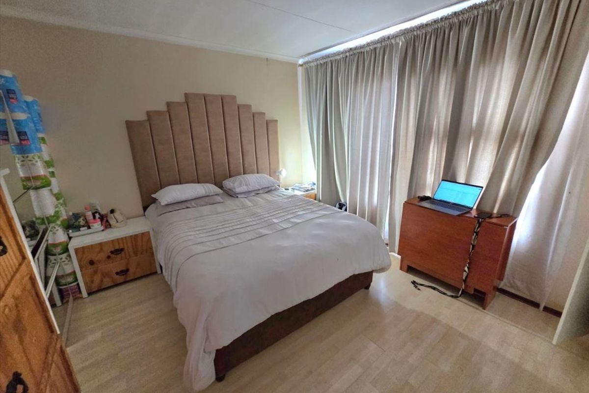 A standard bedroom featuring laminate flooring and floor-to-ceiling curtains, providing a functional space with neutral wall finishes.