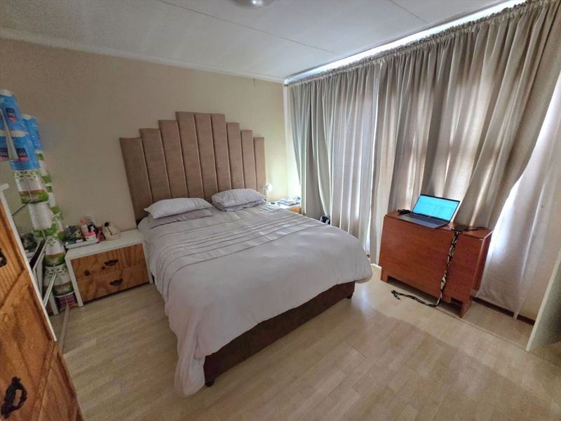 A standard bedroom featuring laminate flooring and floor-to-ceiling curtains, providing a functional space with neutral wall finishes.