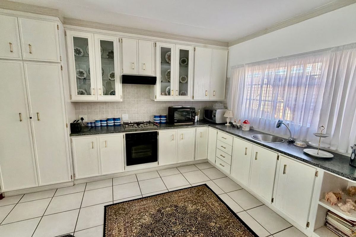A functional kitchen featuring white cabinetry, a gas hob, under-counter oven, tiled flooring, and a stainless steel sink with ample counter space.