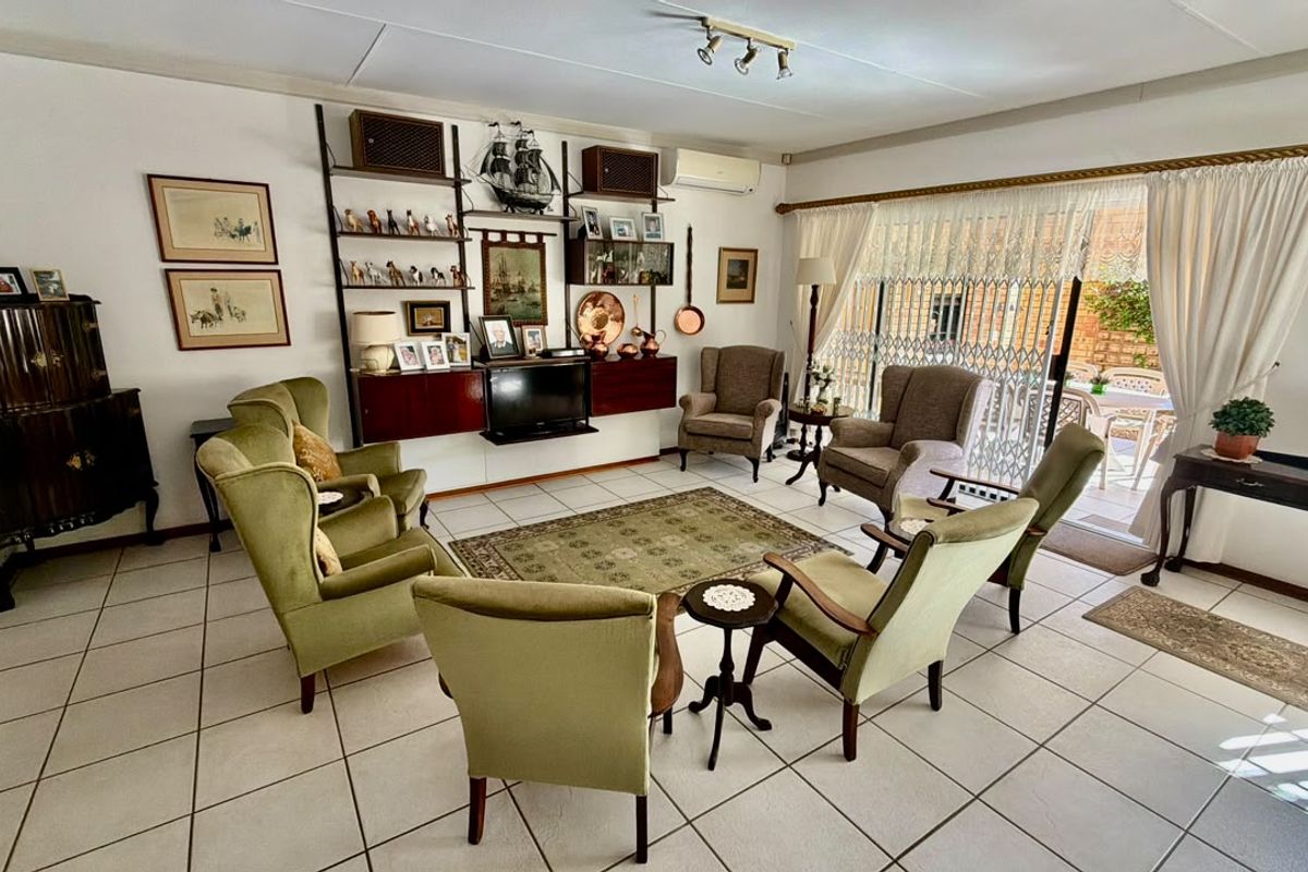 A spacious living room featuring tiled flooring, track lighting, and a sliding glass door providing access to the outdoor patio area.