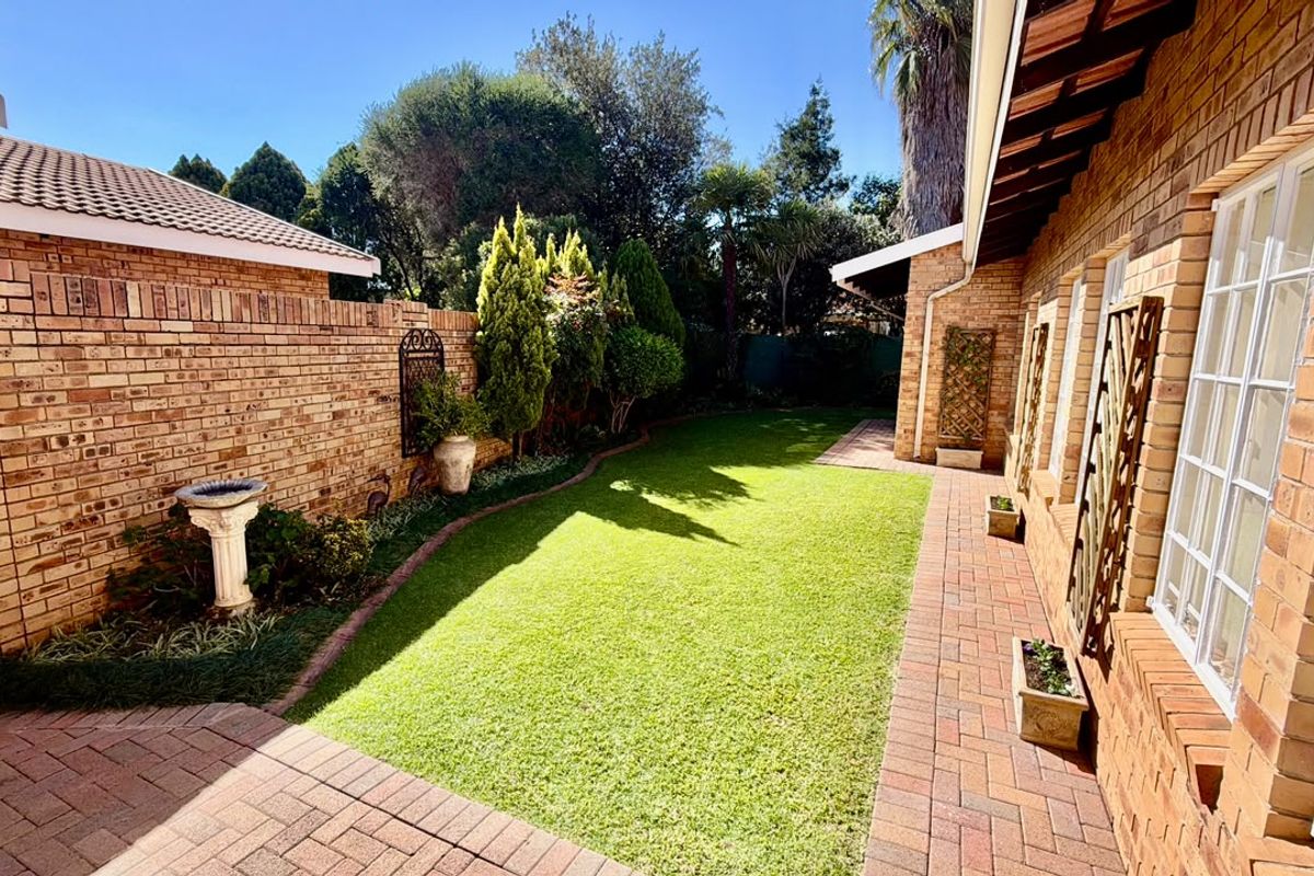 A well-maintained rear garden featuring a manicured lawn, brick paved pathways, and a classic face-brick townhouse exterior with tiled roofing.