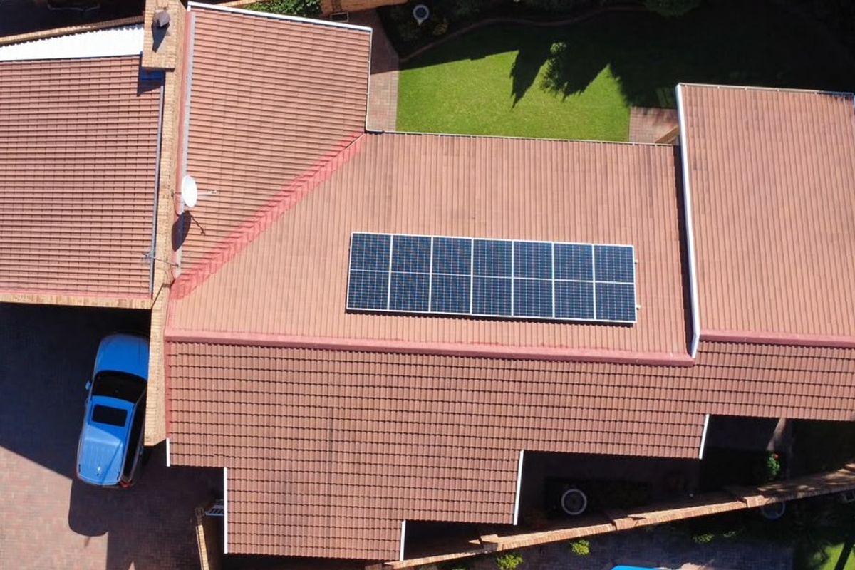 Aerial view of the townhouse property featuring a tiled roof with installed solar panels, a paved driveway, and a landscaped garden area.