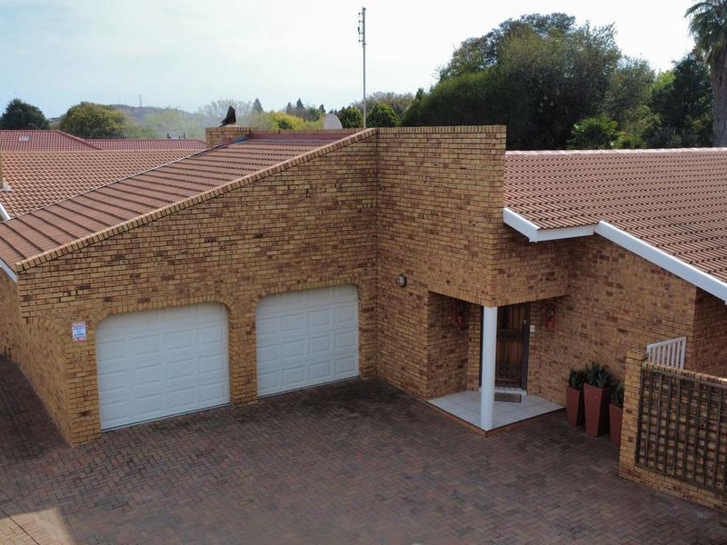 Aerial view of a townhouse exterior featuring a face brick facade, tiled roof, double garage, and a paved driveway.