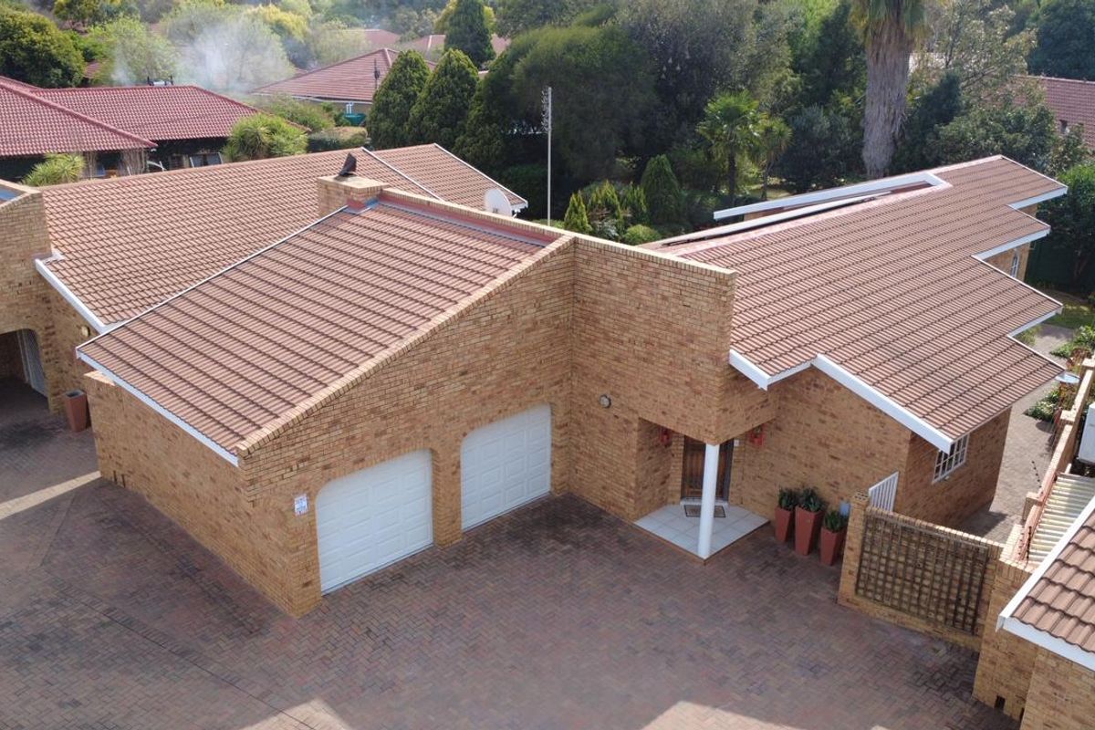 Aerial view of a facebrick townhouse featuring a double garage, tiled roof, and a paved driveway entrance.