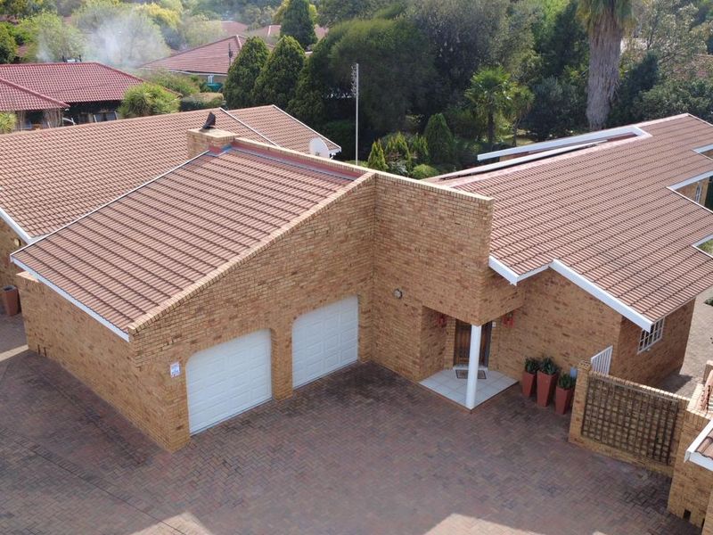 Aerial view of a facebrick townhouse featuring a double garage, tiled roof, and a paved driveway entrance.