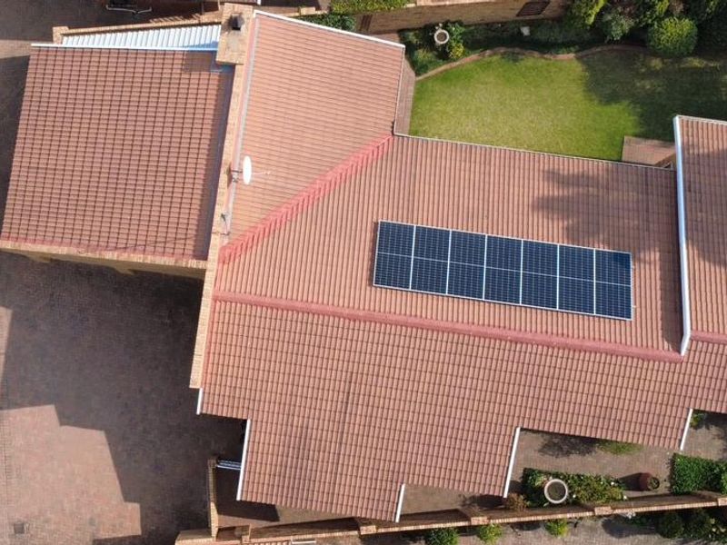 Aerial view of the townhouse property featuring a tiled roof with installed solar panels, a paved driveway, and a private garden area.