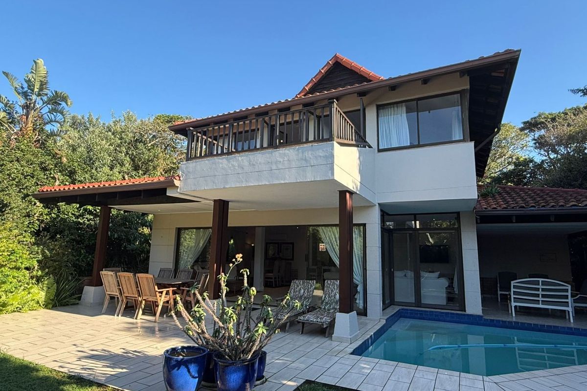 Rear view of a two-story house featuring a tiled patio, swimming pool, and an upper-level balcony with timber railings.