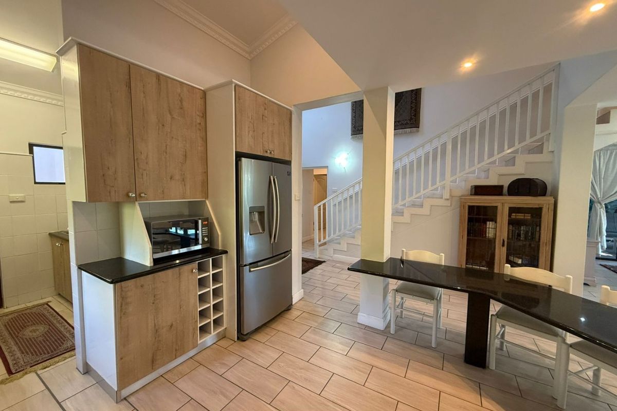 A modern kitchen area featuring wood-finish cabinetry, stone countertops, and a built-in wine rack, seamlessly flowing into an open-plan living space with a staircase.