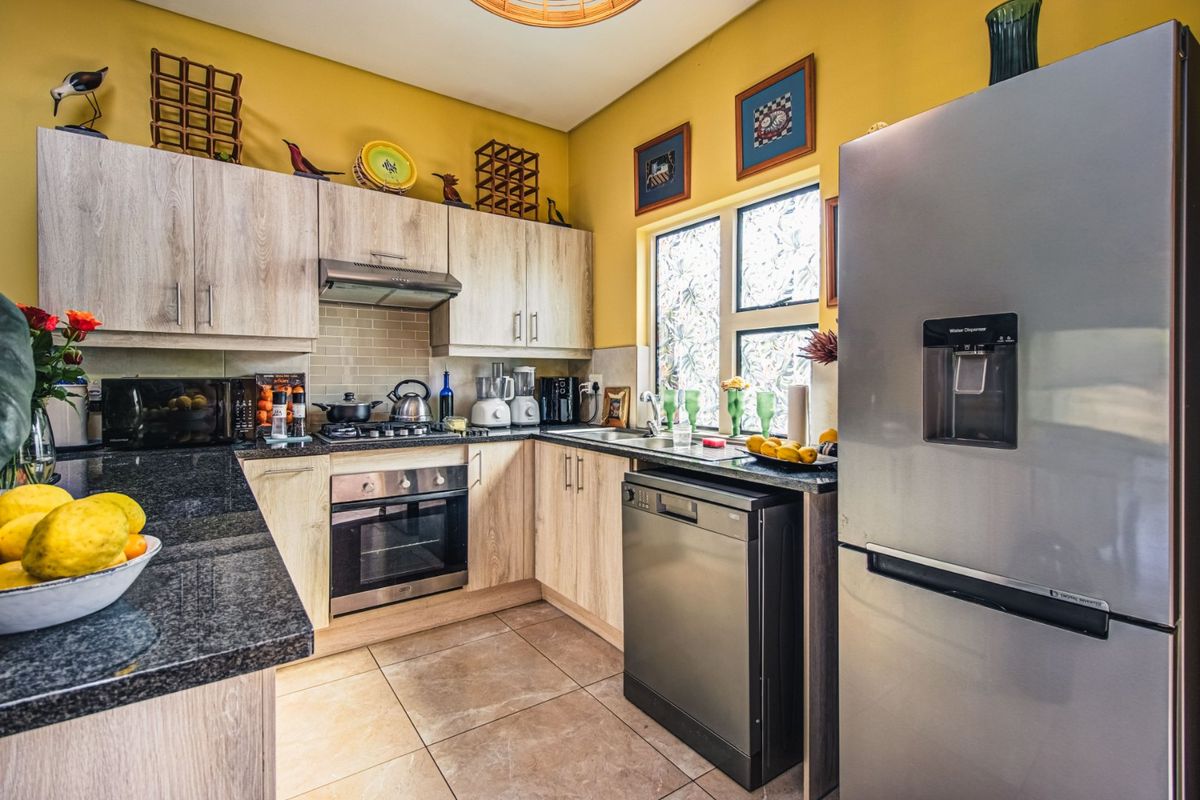 A functional kitchen featuring light wood-look cabinetry, dark granite countertops, built-in oven, gas hob, and tiled flooring with a neutral backsplash.
