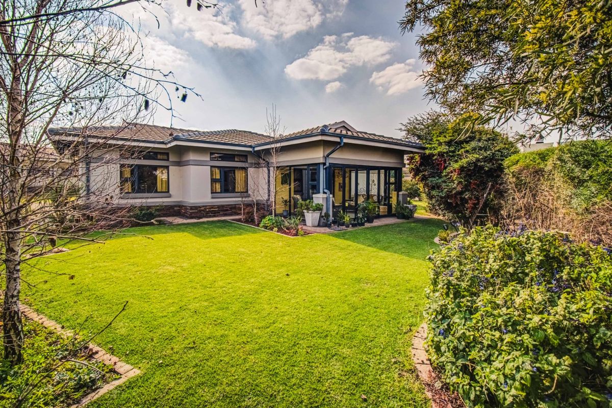 A well-maintained rear elevation featuring a landscaped garden, stone-clad accents, and a covered patio area with large aluminium-framed windows.
