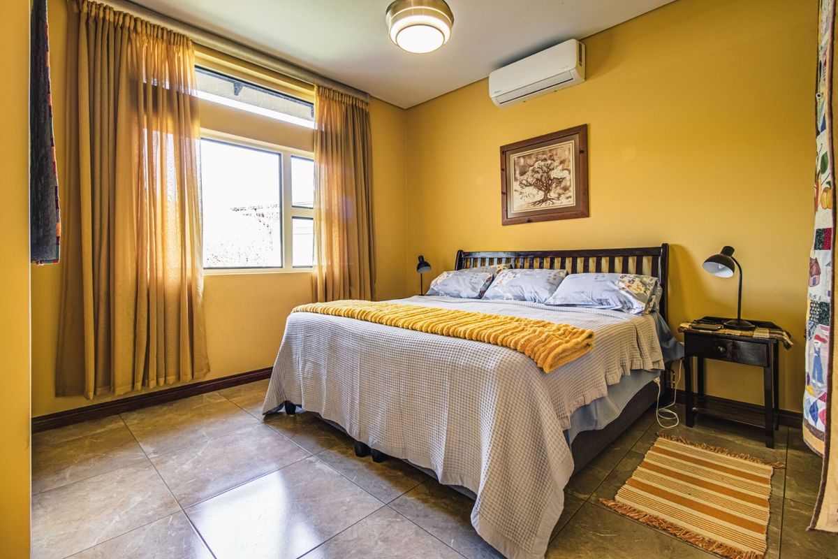 A bedroom featuring tiled flooring, a large window with curtains, and a wall-mounted split-system air conditioner.