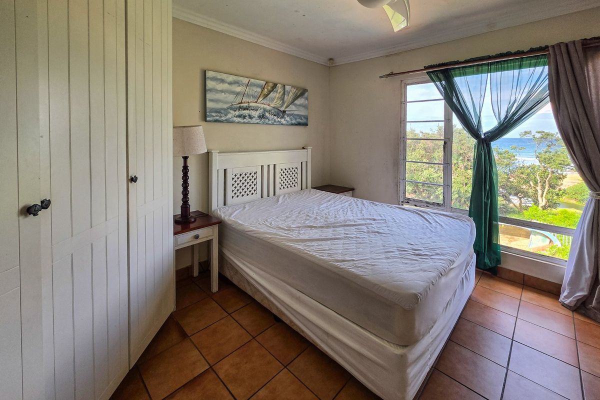 A bedroom featuring built-in wardrobes, tiled flooring, a ceiling fan, and a large window offering scenic coastal views.
