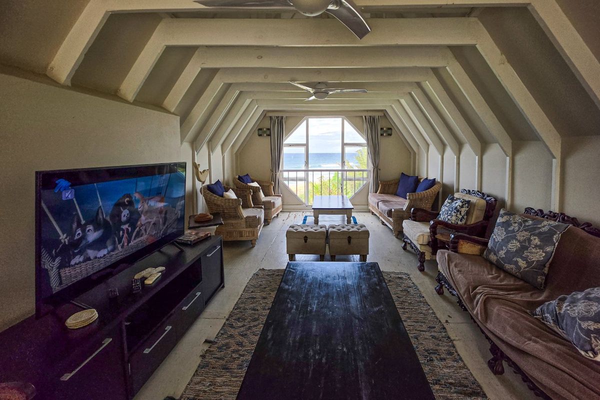Spacious living room featuring unique exposed ceiling beams, dual ceiling fans, and a large window offering scenic ocean views.