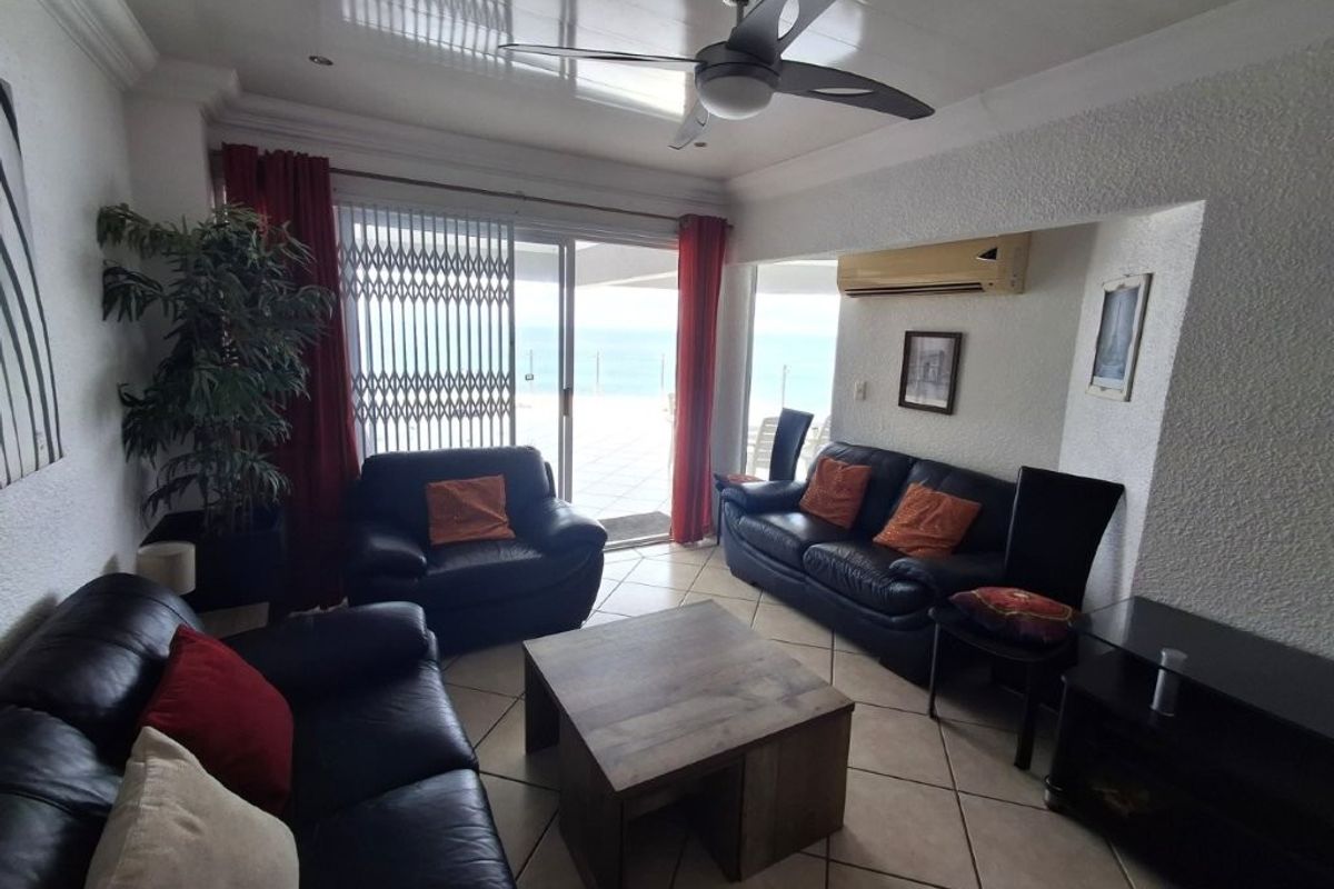 A living room featuring tiled floors, a ceiling fan, and a sliding glass door leading to an outdoor balcony with ocean views.