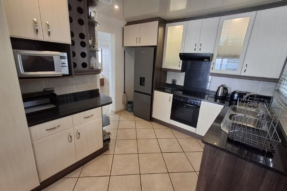 Modern kitchen featuring two-tone cabinetry, granite countertops, built-in oven with extractor fan, and tiled flooring.