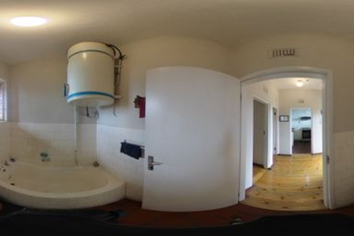 A dated bathroom featuring a built-in bathtub, pedestal basin, and exposed water heater, with timber flooring and tiled wall accents.