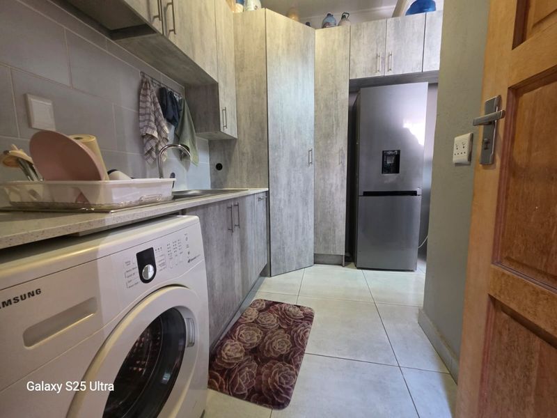 A functional laundry room featuring built-in cabinetry, laminate countertops, a stainless steel sink, and tiled flooring.