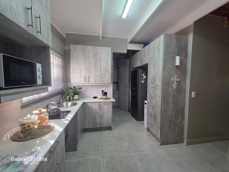 Modern kitchen featuring grey wood-grain cabinetry, laminate countertops, stainless steel sink, and integrated appliances with neutral tiled flooring.