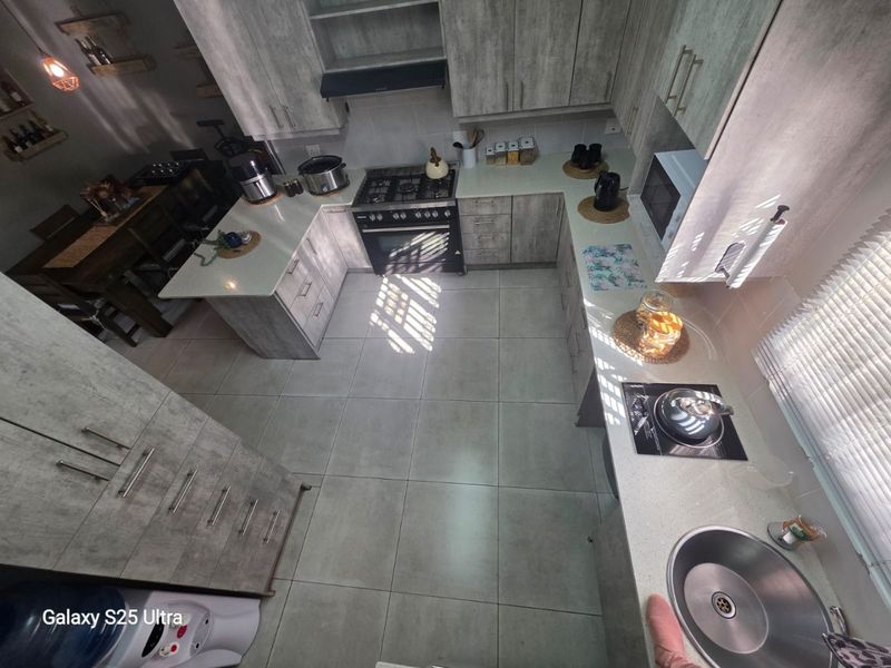 Modern U-shaped kitchen featuring light grey wood-grain cabinetry, stone countertops, a gas stove with extractor, and tiled flooring.