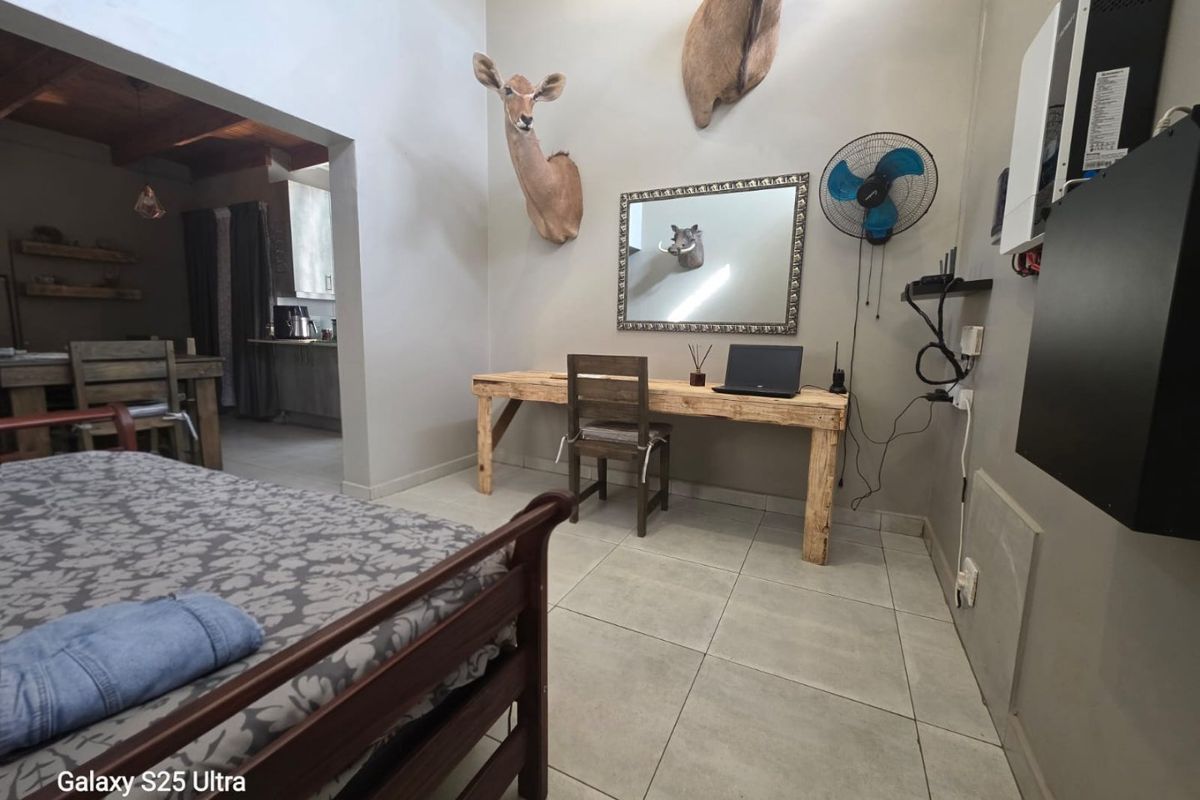 A bedroom featuring tiled flooring and a wall-mounted fan, with an adjacent view into a kitchen area.