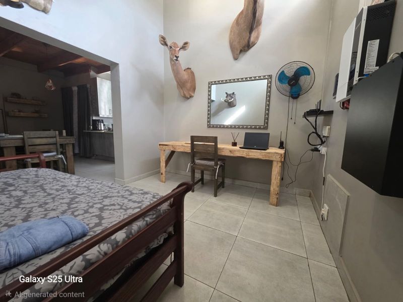 A bedroom featuring tiled flooring and a wall-mounted fan, with an adjacent view into a kitchen area.