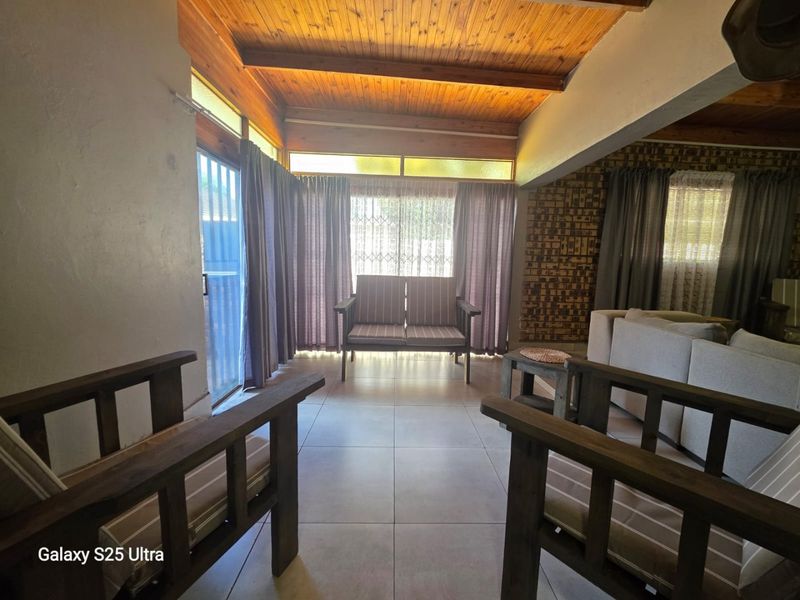 A living area featuring a warm timber beam ceiling, tiled floors, and a brick feature wall, with natural light entering through large sliding doors.