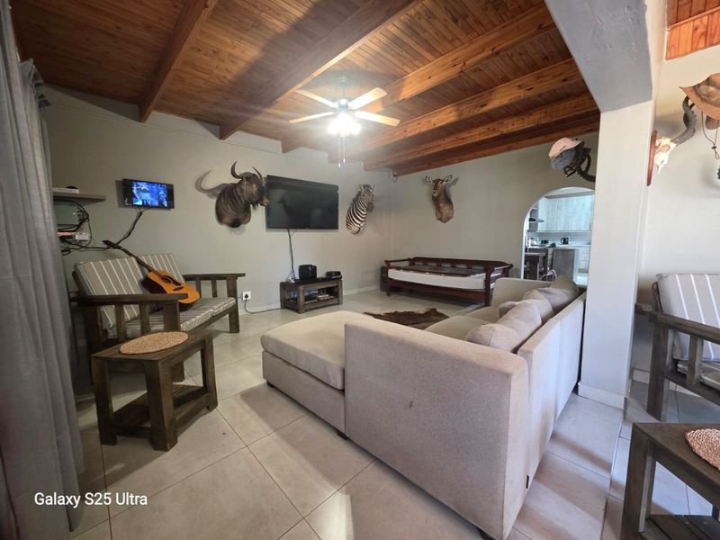 Open plan living area featuring exposed timber beam ceilings, tiled flooring, and an archway leading to the kitchen area.