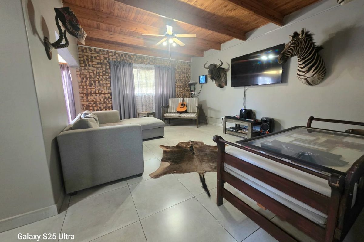 Spacious living room featuring an exposed timber beam ceiling, tiled flooring, and an exposed brick feature wall.