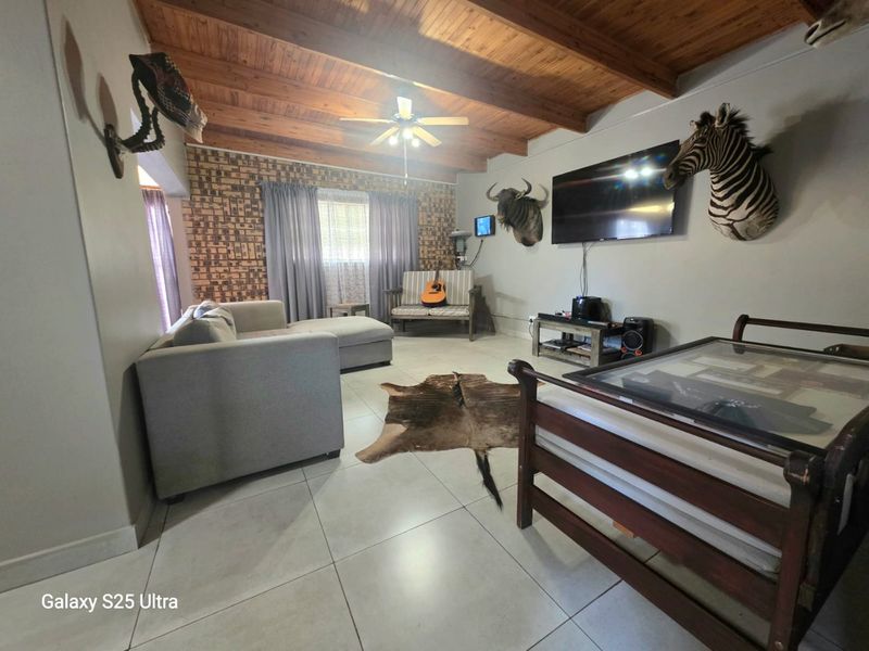 Spacious living room featuring an exposed timber beam ceiling, tiled flooring, and an exposed brick feature wall.