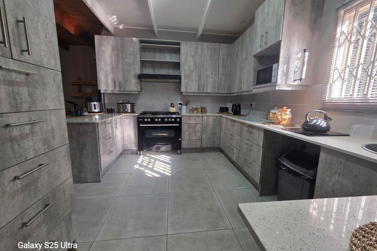 Modern kitchen featuring grey textured cabinetry, stone countertops, a freestanding oven with extractor fan, and tiled flooring.