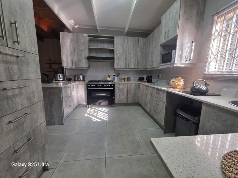 Modern kitchen featuring grey textured cabinetry, stone countertops, a freestanding oven with extractor fan, and tiled flooring.