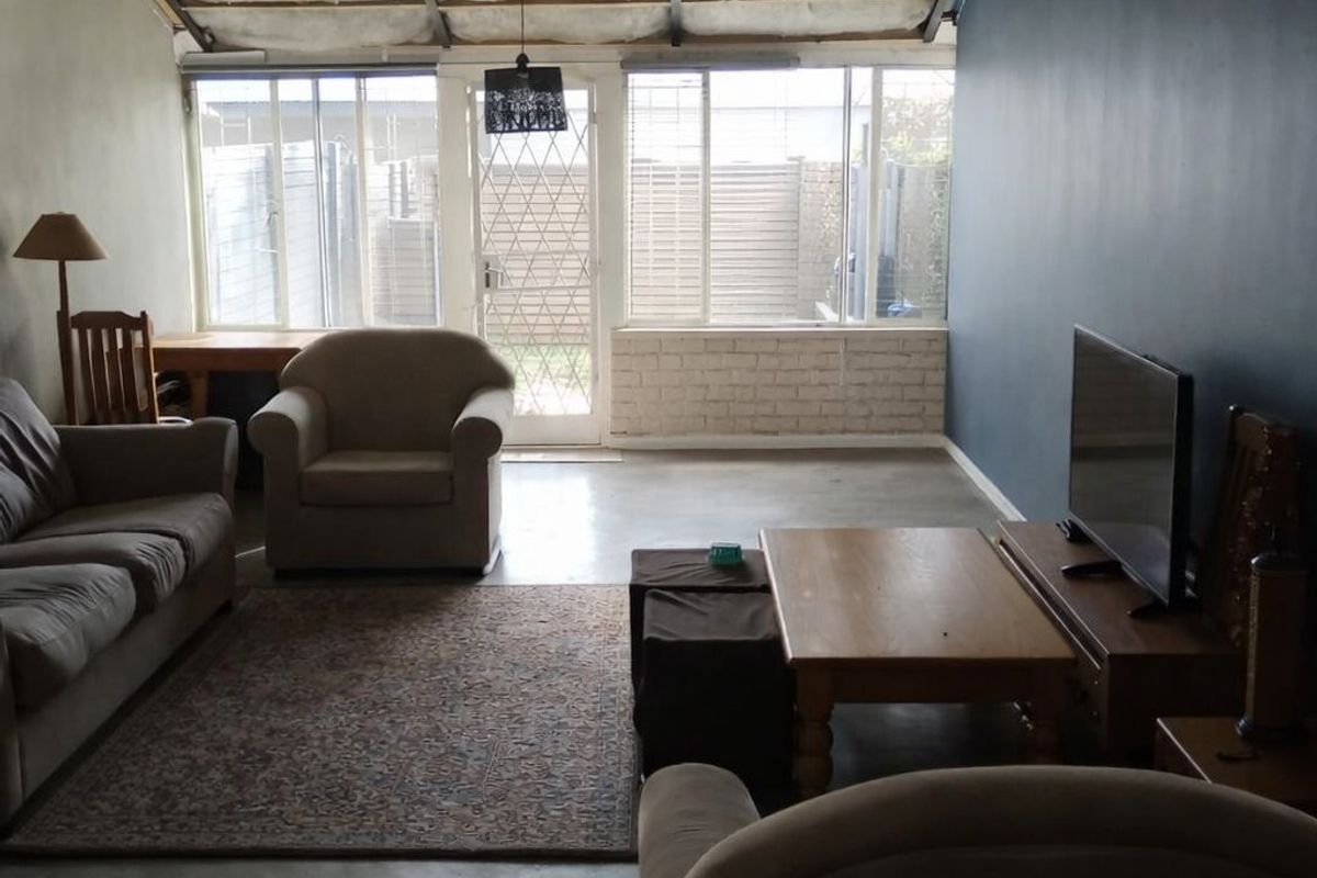 Spacious living area featuring a high raked ceiling with exposed insulation, concrete flooring, and large windows providing natural light and garden access.