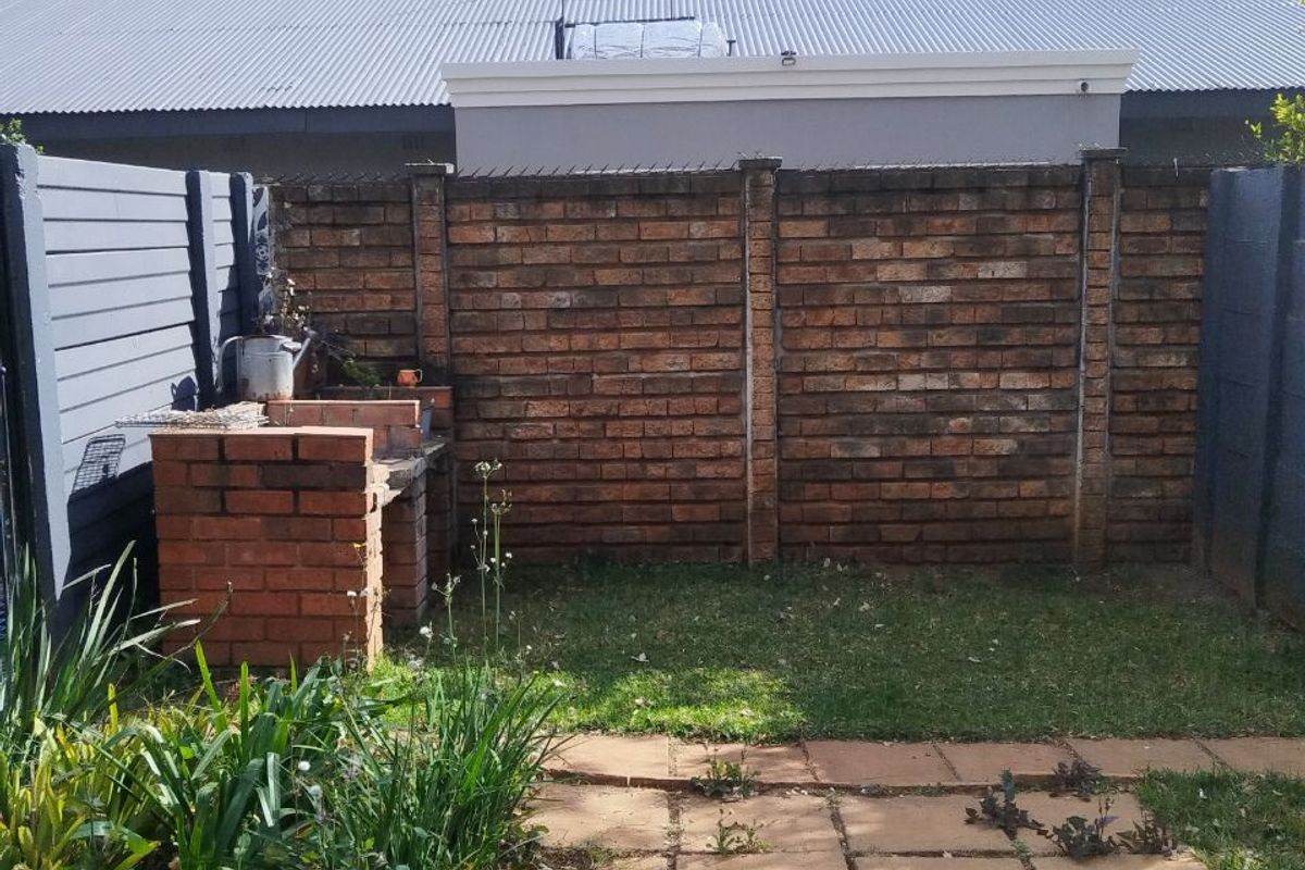 A private rear garden featuring a brick-built outdoor braai, paved patio area, and perimeter brick and timber fencing.