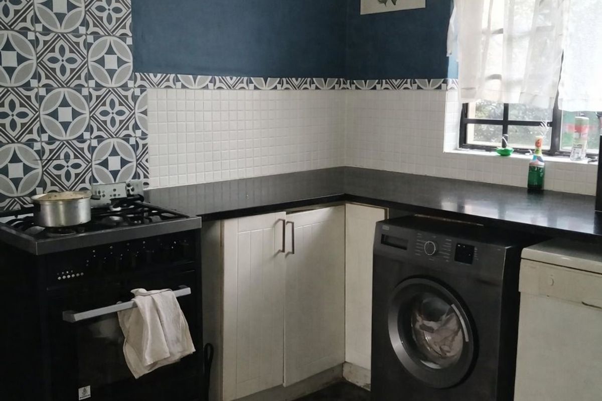 A functional kitchen featuring dark countertops, patterned tile splashbacks, a built-in oven, and dedicated space for laundry appliances.