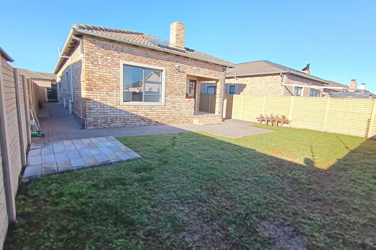 Rear view of a face brick townhouse featuring a paved patio area, chimney, and a private garden enclosed by precast boundary walls.
