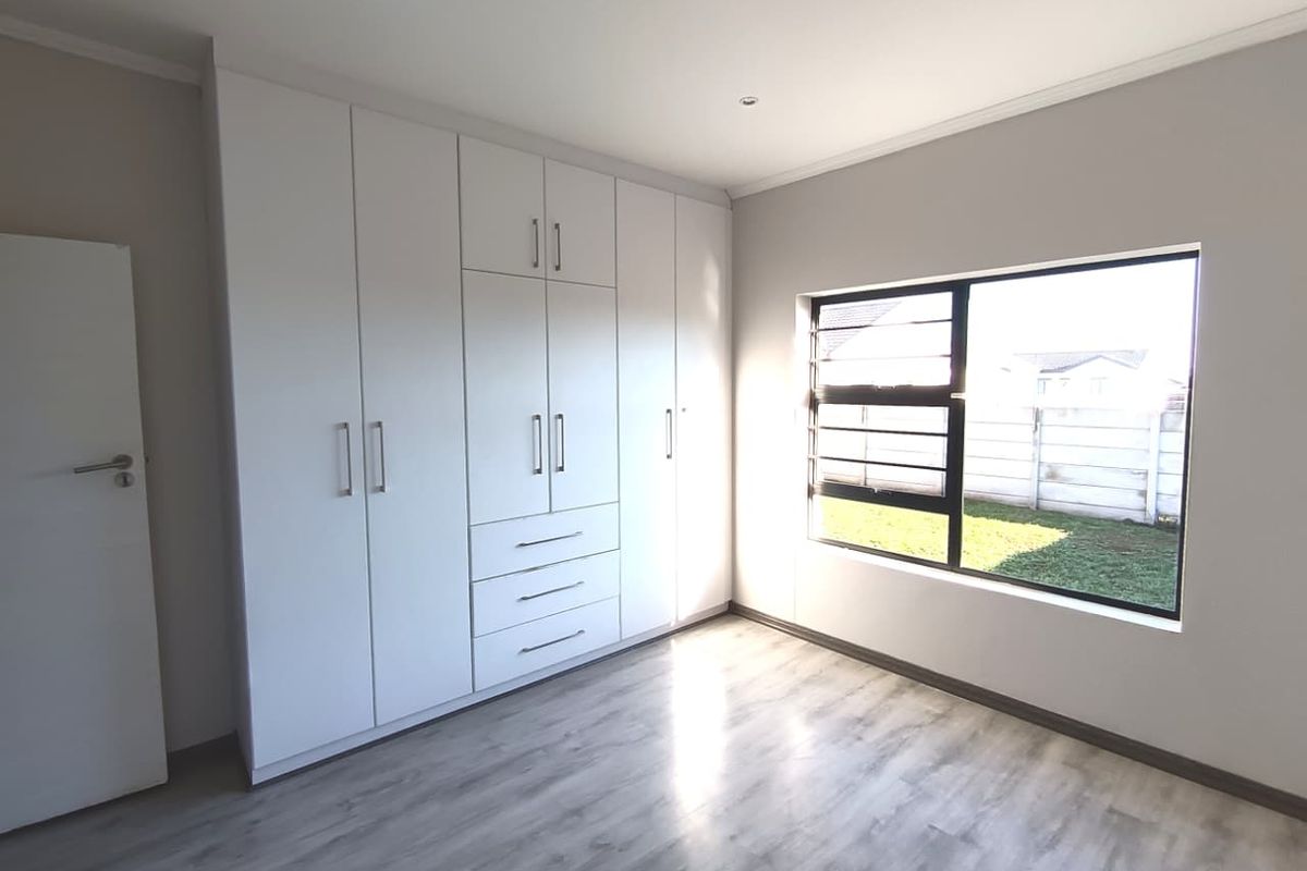 A bright, modern bedroom featuring neutral walls, light wood-look laminate flooring, and extensive built-in cabinetry with ample storage space.