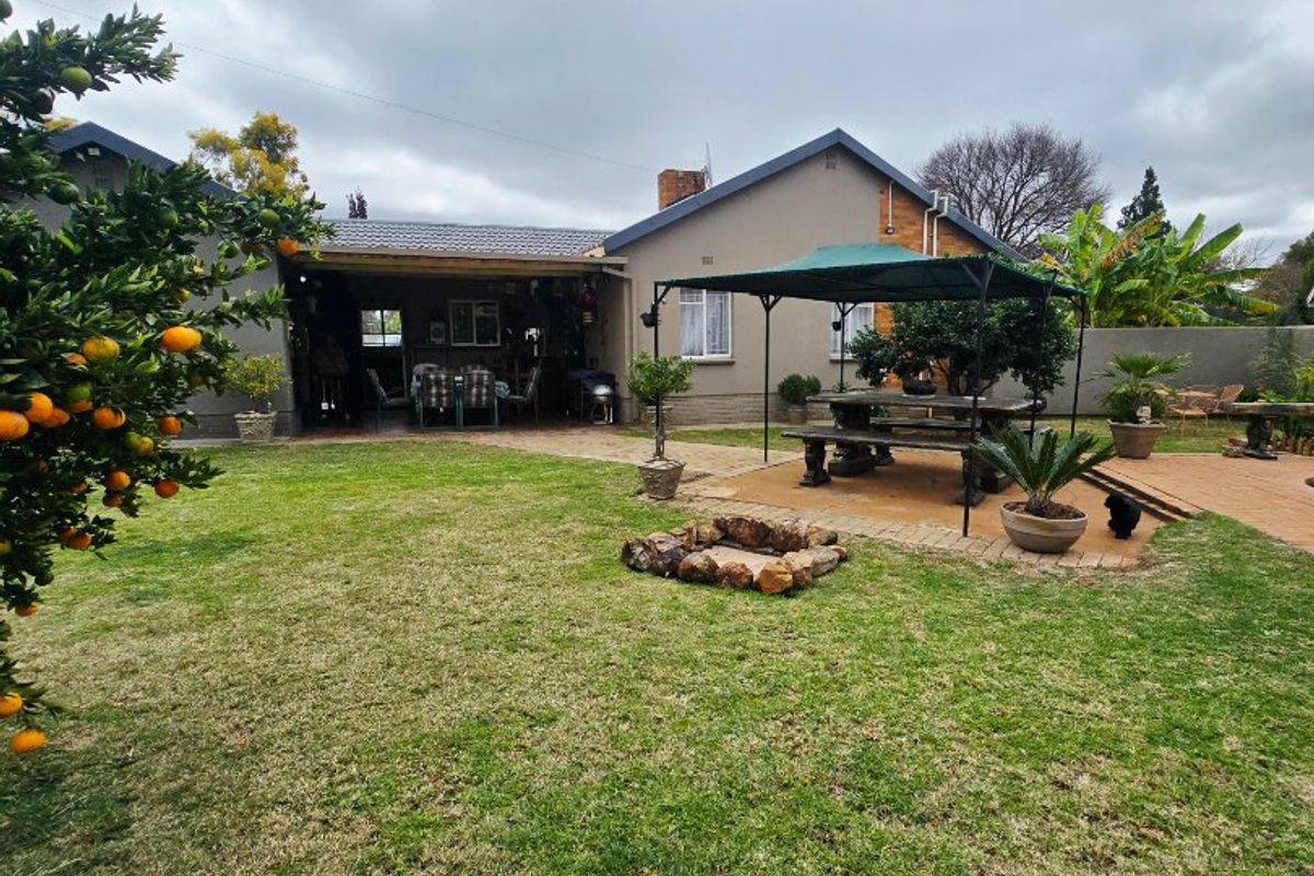 Rear view of the house featuring a covered patio, paved outdoor entertainment area, stone fire pit, and a well-maintained garden.